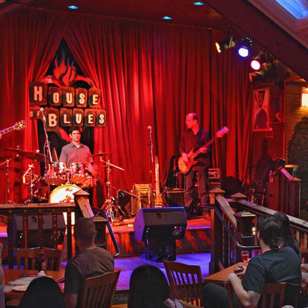 Live band performing on stage under warm lighting at the House of Blues as guests enjoy the show from their tables.