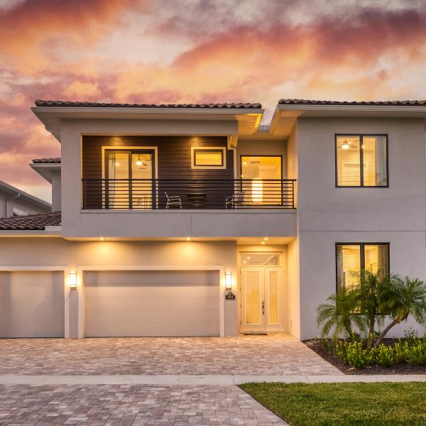 Modern two-story vacation home in Kissimmee at sunset, with warm exterior lighting, a spacious driveway, and an upper-level balcony.