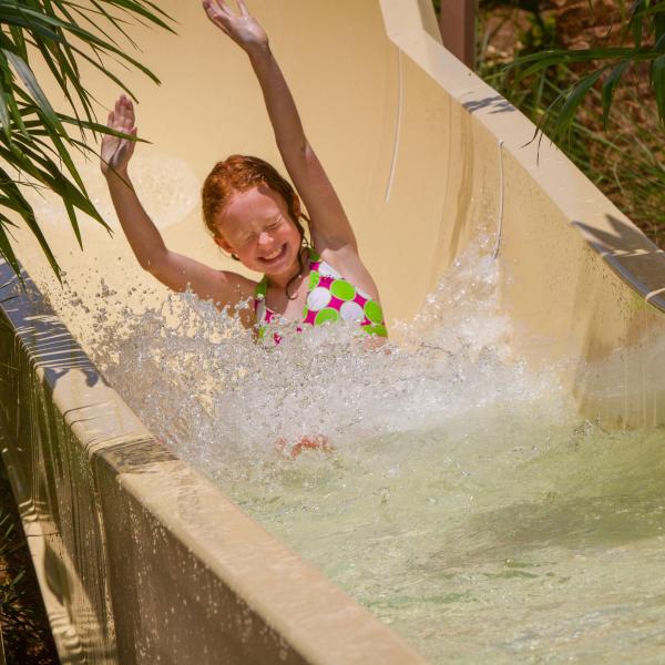 a young girl has her arms outstretched as she speeds down an exciting waterslide.