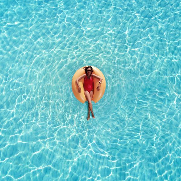 A woman floats in the center of a pool on a yellow donut inflatable. 