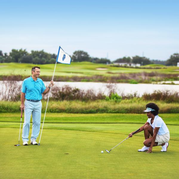 Two golfers on a putting green at a scenic Kissimmee golf course, with one person preparing a putt and another holding the flag.