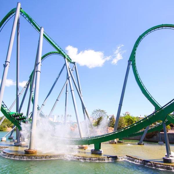 A large green roller coaster travels over water on a sunny day in Kissimmee.
