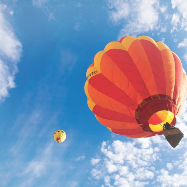 Two hot air balloons—one large and close, one smaller in the distance—float against a bright blue sky with soft, scattered clouds.