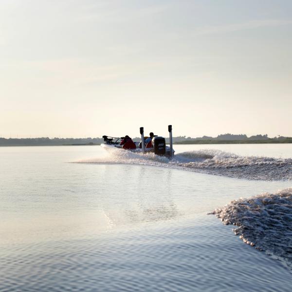 Two anglers ride across the calm waters of Lake Tohopekaliga in a fishing boat during sunrise in Kissimmee, Florida.