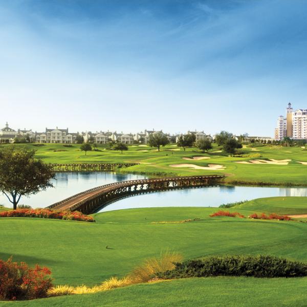 A golf course with a large pond in the middle and a hotel at the opposite end.