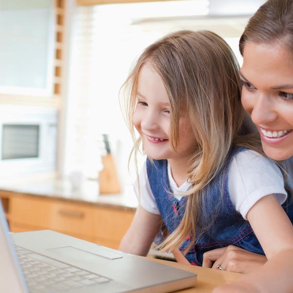 Mother and daughter smiling while planning their next family vacation on a laptop at home.