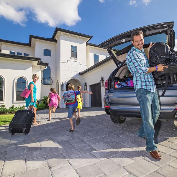 A man unloads his car in front of a vacation home as his family enters the home.