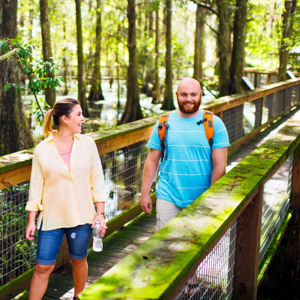 Man and woman walking along a wooden bridge in the woods.