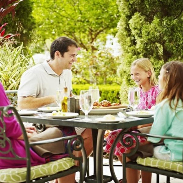 Family dining outdoors at Trevi’s, enjoying a sunny meal together on a garden patio.