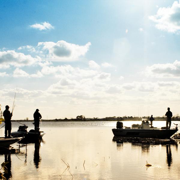 Anglers fishing from boats on a calm lake in Kissimmee, Florida, at sunset, surrounded by trees and golden reflections on the water.