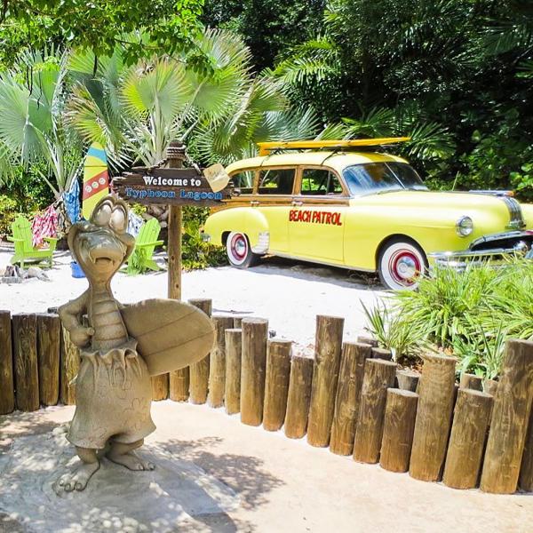 a sign says 'welcome to typhoon lagoon' with a yellow beach patrol car in the background.