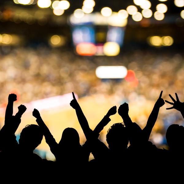 Backlit silhouettes of fans cheering at a basketball game.