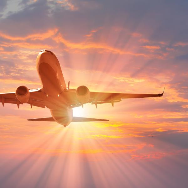 An airplane takes off into a colorful sunset sky with rays of sunlight streaming behind it.