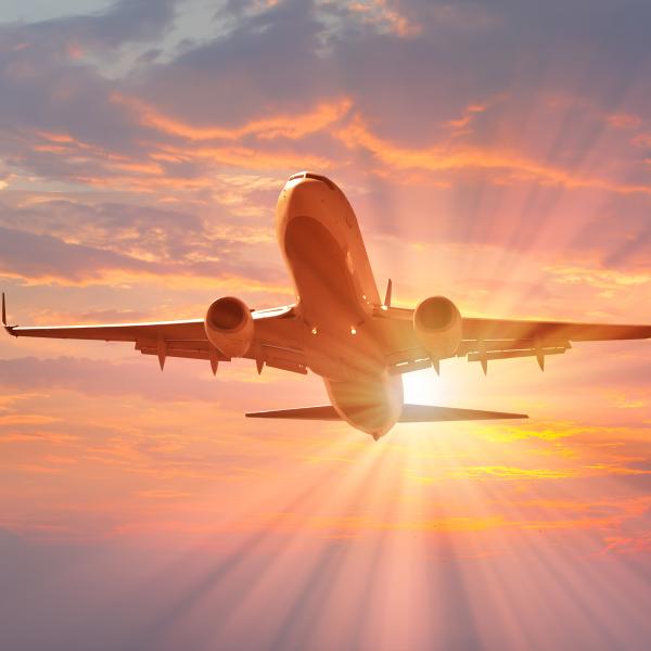 An airplane takes off into a colorful sunset sky with rays of sunlight streaming behind it.