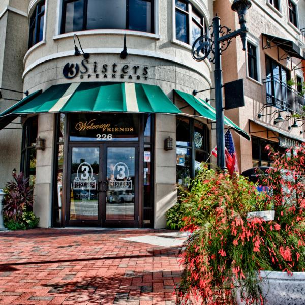Exterior of 3 Sisters Speakeasy restaurant in Downtown Kissimmee, Florida, featuring a green awning, outdoor seating, and a welcoming entrance.