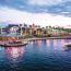 Evening view of Universal CityWalk in Orlando, Florida, with colorful lights reflecting on the water and a boat cruising along the canal near restaurants and entertainment venues.