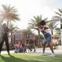 Families enjoying outdoor entertainment at Promenade at Sunset Walk in Kissimmee, Florida, with a woman and young girl hula-hooping under palm trees on a sunny afternoon.
