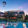 Evening view of Disney Springs with the iconic Aerophile balloon floating above the Springs Bottling Co. building, surrounded by palm trees and water reflecting the sunset sky.